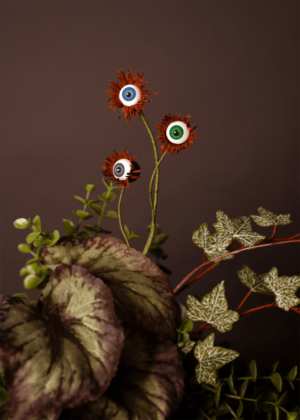 Three fake eyeball garden decorations with spiky orange-brown fringe and green foliage, arranged against a dark grey background.