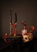 Gothic creature arrangement featuring red thread eyeball vines with green brown leaves draped around a skull, candlesticks, a glass bottle, and a dark cloth against a dark brown background.