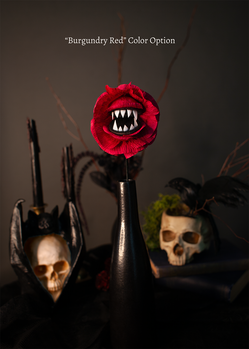 A gothic-style product photo featuring a dark red rose with a fanged mouth design in a black vase, with decorative skulls and black elements in the background. Text at the top reads “*Burgundy Red’ Color Option.
